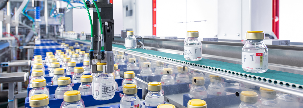 A robotic gripper arm carefully and safely picks up a delicate glass bottle containing human plasma preparation and positions it onto a conveyor belt.